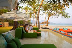 two people sitting on a couch under an umbrella on the beach at Tolani Resort Koh Samui in Lamai