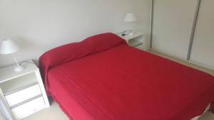 Cama roja en habitación blanca con mesita de noche en Departamento Solar del Parque en Necochea