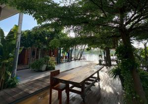 Ein Holztisch und Bänke auf einer Terrasse mit Bäumen in der Unterkunft Amphawa Hideaway in Amphawa