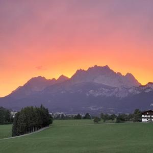 a sunset over a green field with mountains in the background at Sonnseit in Sankt Johann in Tirol