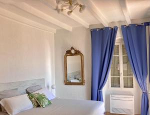ein Schlafzimmer mit einem Bett, blauen Vorhängen und einem Spiegel in der Unterkunft Solacargese-Le Jardin d'Irène-Vue panoramique exceptionnelle sur la Méditerranée in Cargèse