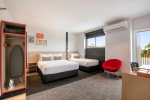 um quarto de hotel com duas camas e uma cadeira vermelha em Nightcap at Camp Hill Hotel em Brisbane