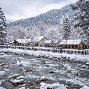 a river with snow on the ground next to buildings at River Retreat Resort in Pahalgām