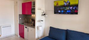 a kitchen with pink cabinets and a blue couch in a room at Cap Esterel, quartier Belvédère 2p meublé tourisme 3 étoiles climatisé Rez-de-Jardin, Vue Mer, WIFI, Piscine et Parking inclus in Agay - Saint Raphael