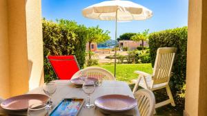 a table with wine glasses and an umbrella at Cap Esterel, quartier Belvédère 2p meublé tourisme 3 étoiles climatisé Rez-de-Jardin, Vue Mer, WIFI, Piscine et Parking inclus in Agay - Saint Raphael