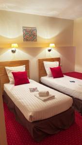 two beds in a hotel room with red pillows at Hotel Des Voyageurs in Le Rouget