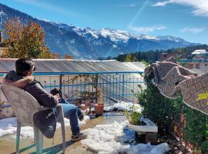 a man sitting on a chair on a balcony at Negi Wooden House in Manāli