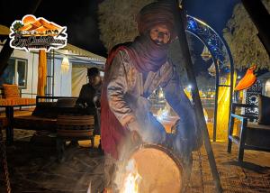 a woman is cooking in a pot over a fire at Erg Chebbi Dunes Desert Camp in Merzouga