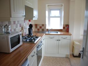 a kitchen with white cabinets and a stove and a microwave at Shallcross Hall Cottage - Toddbrook - Whaley Bridge in Taxal