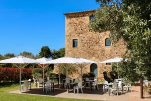 a patio with tables and white umbrellas in front of a building at Hotel Restaurant Mas Roig - Adults only in Pals
