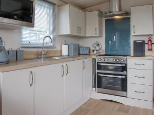 a kitchen with white cabinets and a stove top oven at Premier Caravan 10 in Tywyn