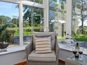 a wicker chair sitting in a room with windows at Horsepark Cottage in Girthon
