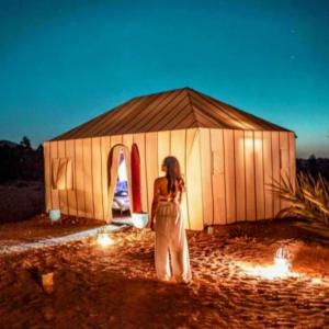 a woman standing in front of a wooden tent at Sunset Dunes Luxury Camp in Merzouga