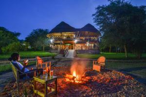 a woman sitting by a fire in front of a building at Elephant View Lodge in Kasenyi