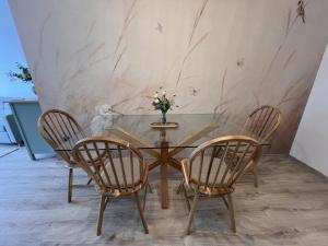 a glass table with three chairs and a vase with flowers at Olive II Apartman in Alsóörs