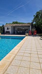 a swimming pool with two red chairs and a house at Cocooning et Charmante Maisonnette Provençale, avec Extérieurs privatifs et Accès Piscine in Orgon