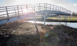a bridge over a river with the sun shining on it at De Kazerne - Beulaker wijde in Wanneperveen