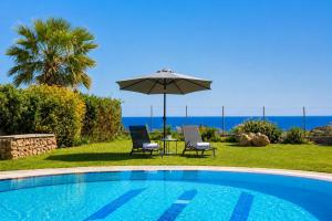 a swimming pool with two chairs and an umbrella at Villa Driftwood in Rhodes Town