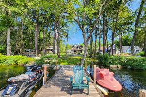 a dock with two chairs and boats on a river at Yellow Door Cottage in Meredith