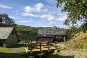 a barn with a bridge in front of a house at Cwm Clyd Longhouse in Llanwrthwl