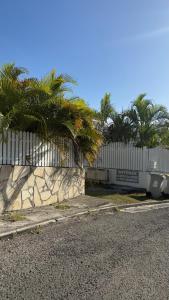 a fence with palm trees in front of a building at Peace's House, Studio moderne, Bas-du-Fort, Plage à pied, Parking privé in Le Gosier