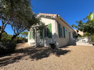 a small white house with green shutters on a gravel driveway at Adorable maison de vacances plain pied au coeur de la station et proche des plages 4 chambres, jardin, WIFI, LXDUNE1 in Portiragnes