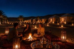 a group of people sitting around a fire at night at Erg Chebbi Sahara Camp in Merzouga