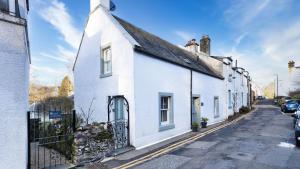 a white house with a black roof on a street at Pear Tree Cottage, Dunblane in Dunblane