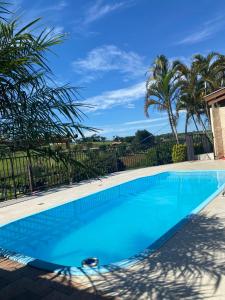 a swimming pool with blue water and palm trees at Casa Star - Vista para as Montanhas in Monte Sião