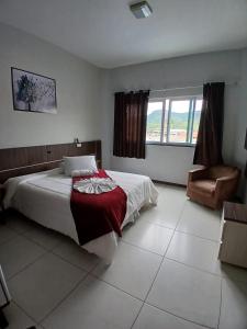 a bedroom with a bed and a chair and window at Miotto Executive Hotel in Navegantes