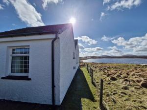 a white building on the shore of a body of water at Lochan View Cottage in Breaclete
