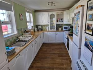 a kitchen with white cabinets and wooden floors at Lochan View Cottage in Breaclete