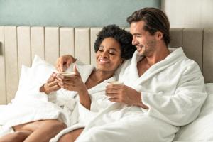a man and woman sitting in bed looking at their phones at The Clayfield, in the Unbound Collection by Hyatt in Niagara-on-the-Lake