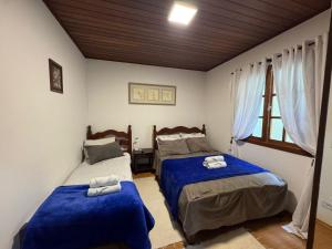 a bedroom with two beds with blue sheets and a window at Pousada D' Paula in Campos do Jordão