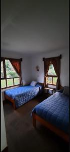 two beds in a room with two windows at Cabañas El Nuevo Cimarrón in Puerto Varas