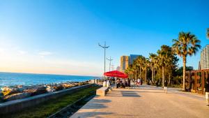 a sidewalk next to the ocean with palm trees and a red umbrella at Nautilus Apartment in Batumi