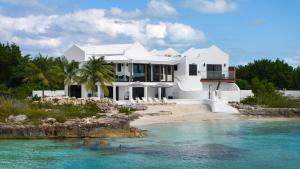 a white house on a beach next to a body of water at Opaline Villa 4BR 2Bath-Ocean Front in Providenciales