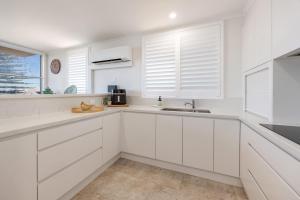 a white kitchen with white cabinets and a sink at Beach Street Oasis - Tuncurry in Tuncurry