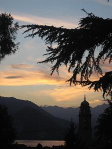 une tour d'horloge avec un coucher de soleil dans les montagnes dans l'établissement Ostello Verbania, à Verbania