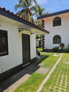 a white house with a black door and grass at Habitaciones Casa Cuscatlan in Tamanique