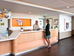 a woman standing at a reception counter in a waiting room at ibis budget Brugge Centrum Station in Bruges