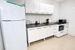 a kitchen with white cabinets and a white refrigerator at Flat 2 quartos em residencial | Ar e garagem in Ourinhos