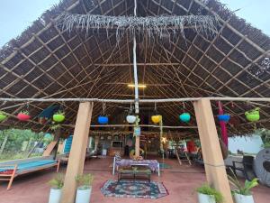 a patio with a straw roof with a table and chairs at WoodPacker Hostel Auroville Pondicherry in Auroville +55 photos
