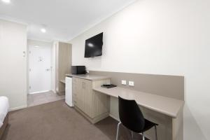 a room with a desk and a bed and a television at Beachside Boutique Motel Mackay in Mackay