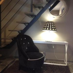 une chaise noire assise sous un escalier avec une lampe dans l'établissement La Dolce Vita, à Jeuxey