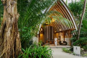 a man walking through a building with a palm tree at Kandolhu Maldives in Mushimasgali