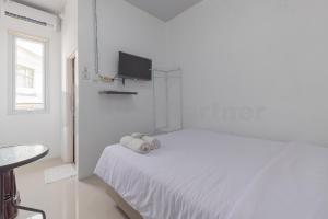 a white bedroom with a bed with a tv on the wall at Adam Guesthouse Mitra RedDoorz in Bogor