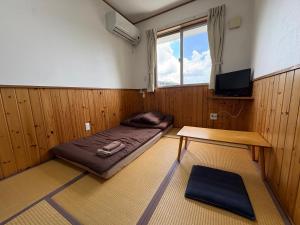 a room with a bed and a table and a tv at Hostel Mosura no Tamago in Motobu