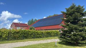 a house with solar panels on the roof and a tree at Ferienhof Harlenest in Wittmund +9 photos