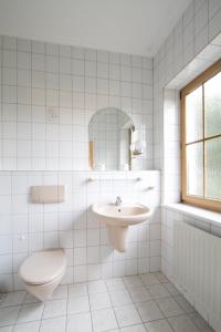 a white tiled bathroom with a toilet and a sink at Hotel Gröbern am See in Gröbern